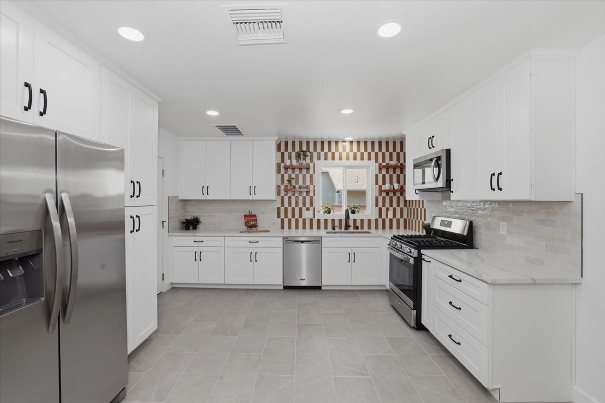 Full view of a white kitchen with an orange-and-white checkerboard tile wall, stainless refrigerator, range and dishwasher