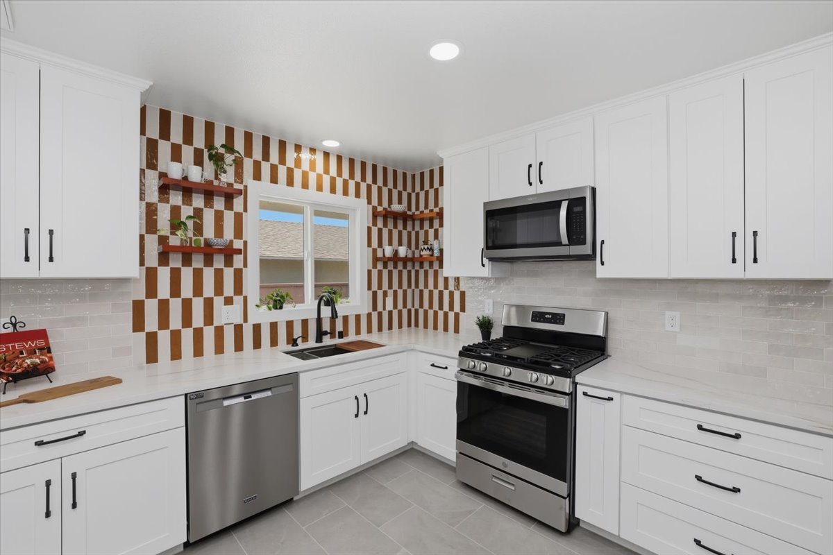 White kitchen with an orange-and-white checkerboard tile wall, open wood shelves, stainless range and dishwasher