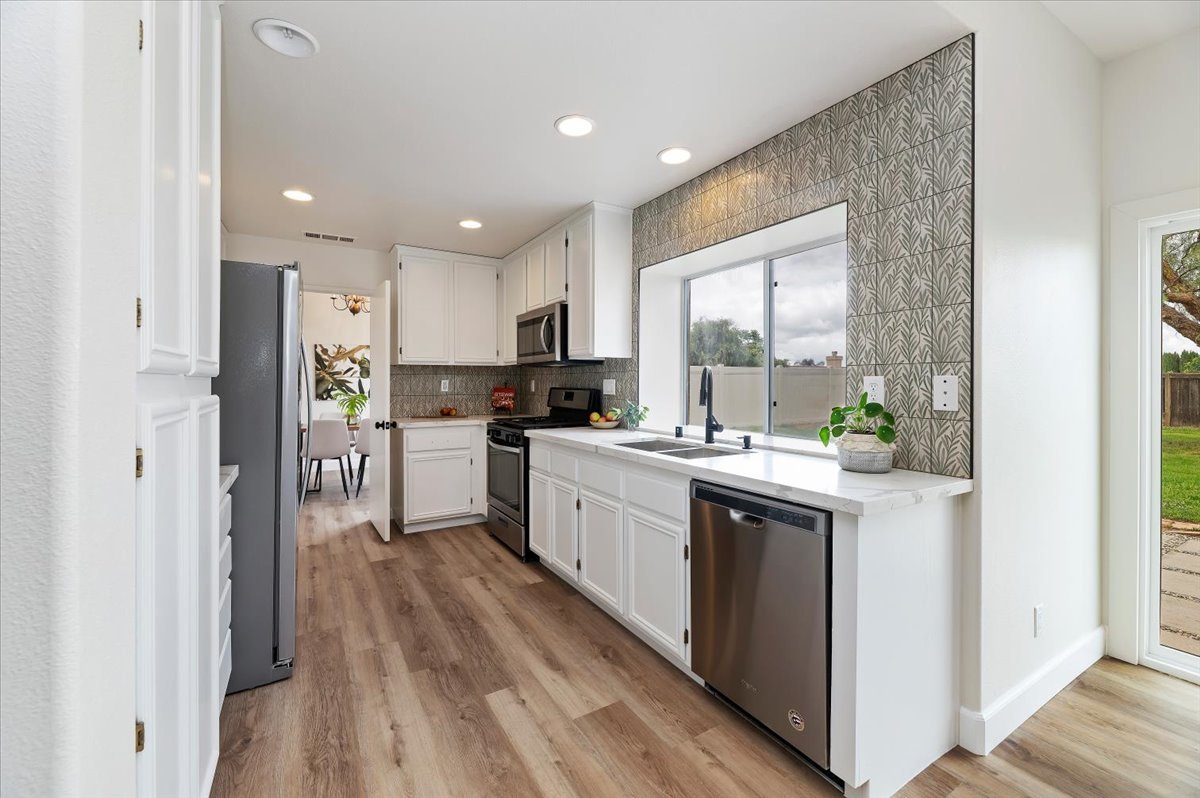 White galley kitchen with a green leaf-pattern tile wall, quartz counters, stainless appliances and wood-look floors