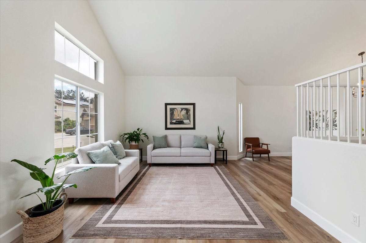 Staged living room with vaulted ceiling, two white sofas, a bordered area rug and potted plants